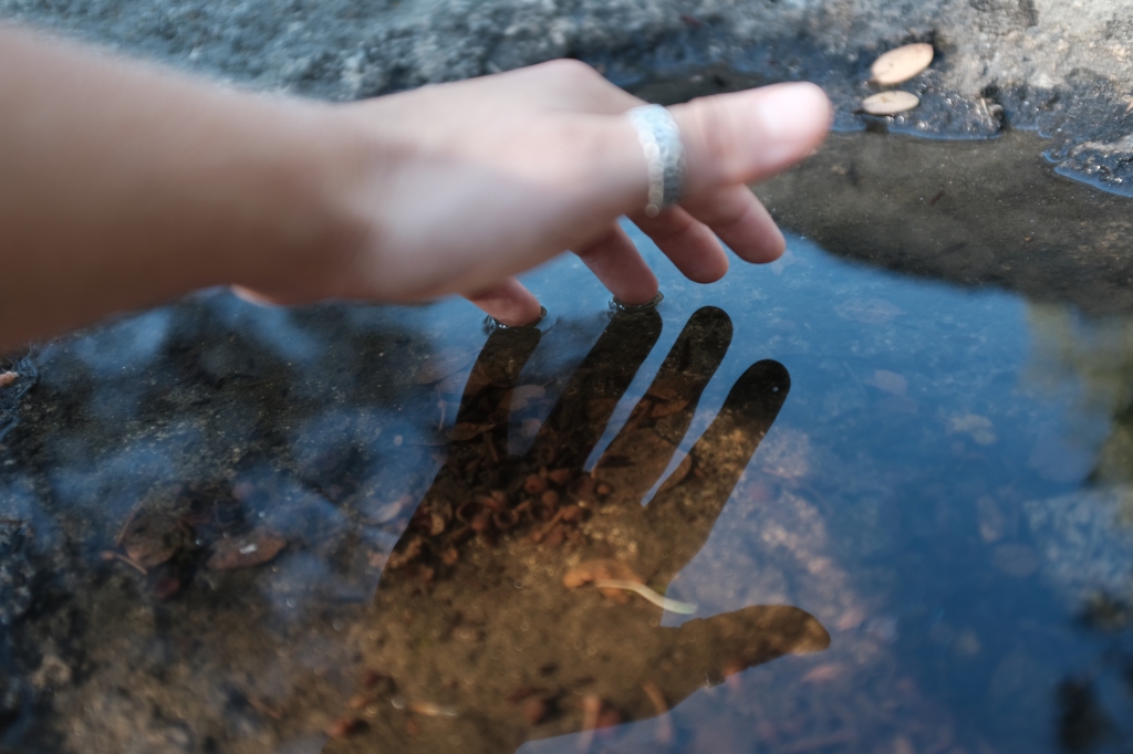 Hand over top of a pool of water with the reflection of the hand in focus.