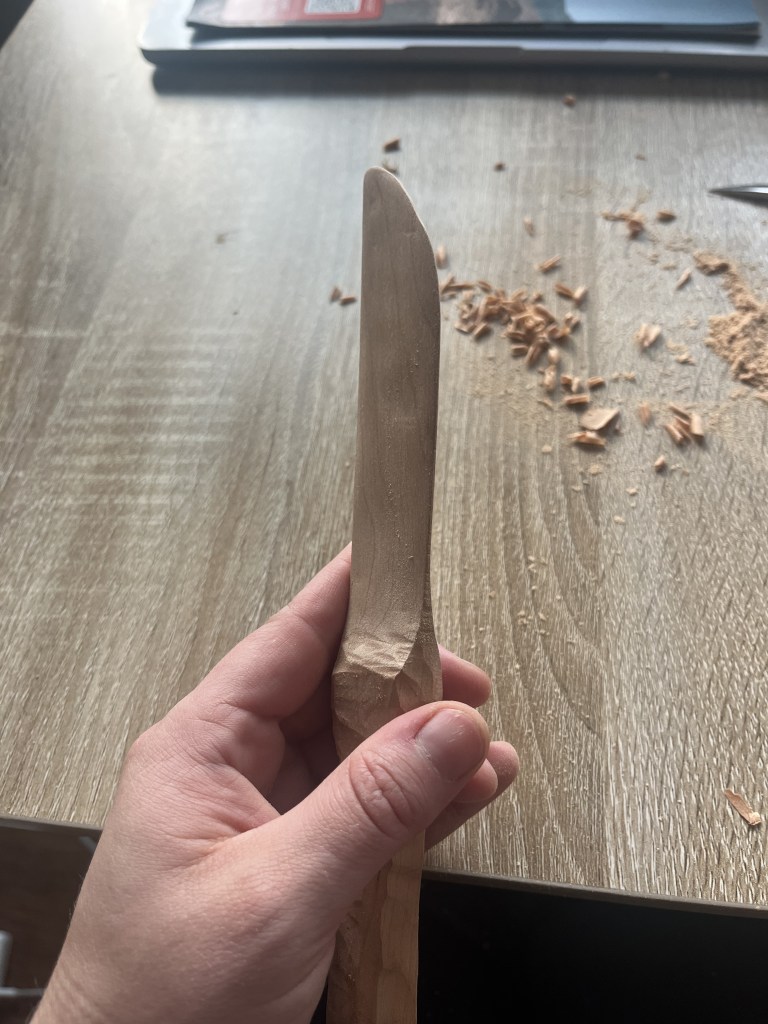 Hand holding a wooden knife mid carving.