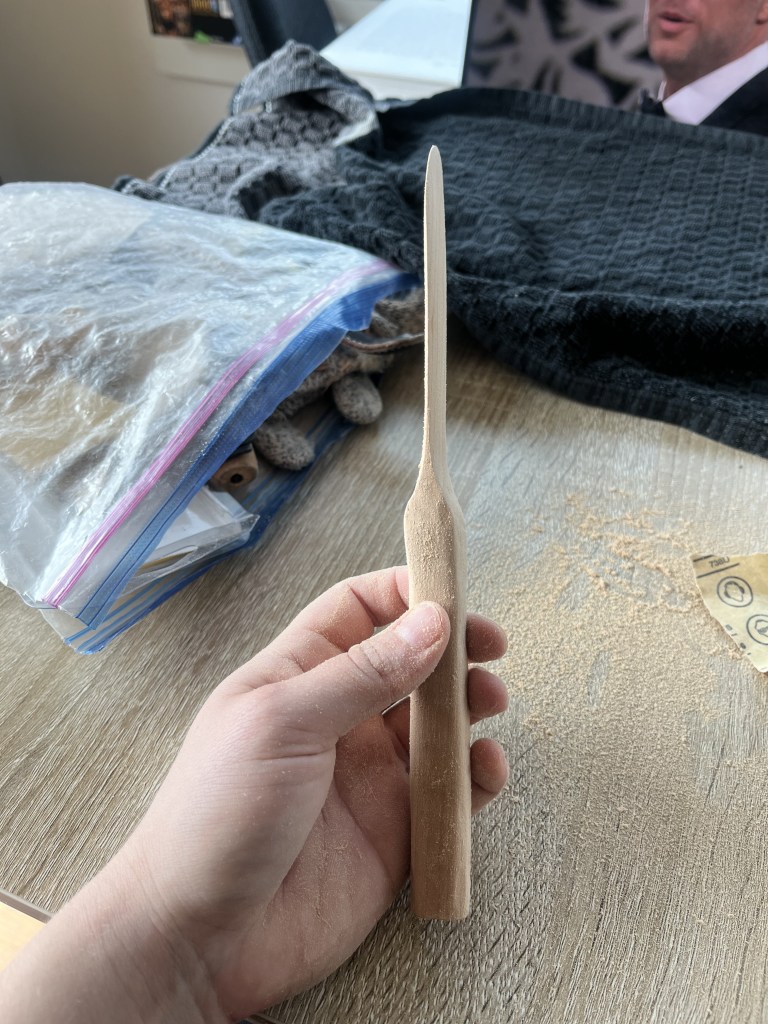 Hand holding a wooden knife showing the blade directly in the middle of a sanding session.