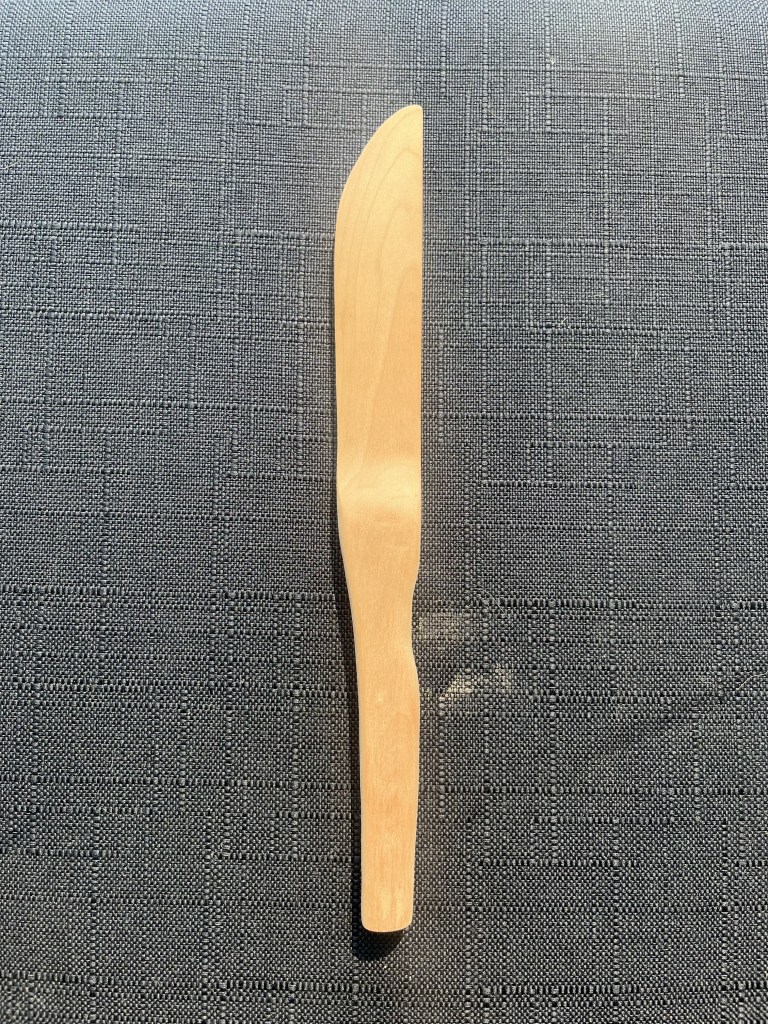White wooden knife before it's been sealed flat on a surface against a black background.