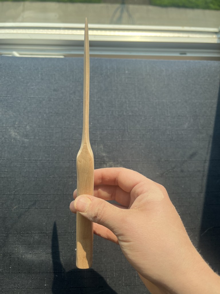 Hand holding a more white wooden knife before it's been sealed showing the blade directly against a black background.