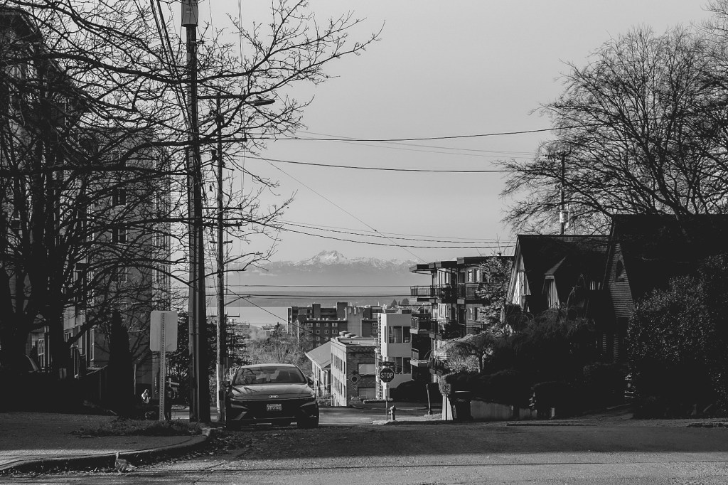 Mountain ranges shown in the distance down a city street in black and white.